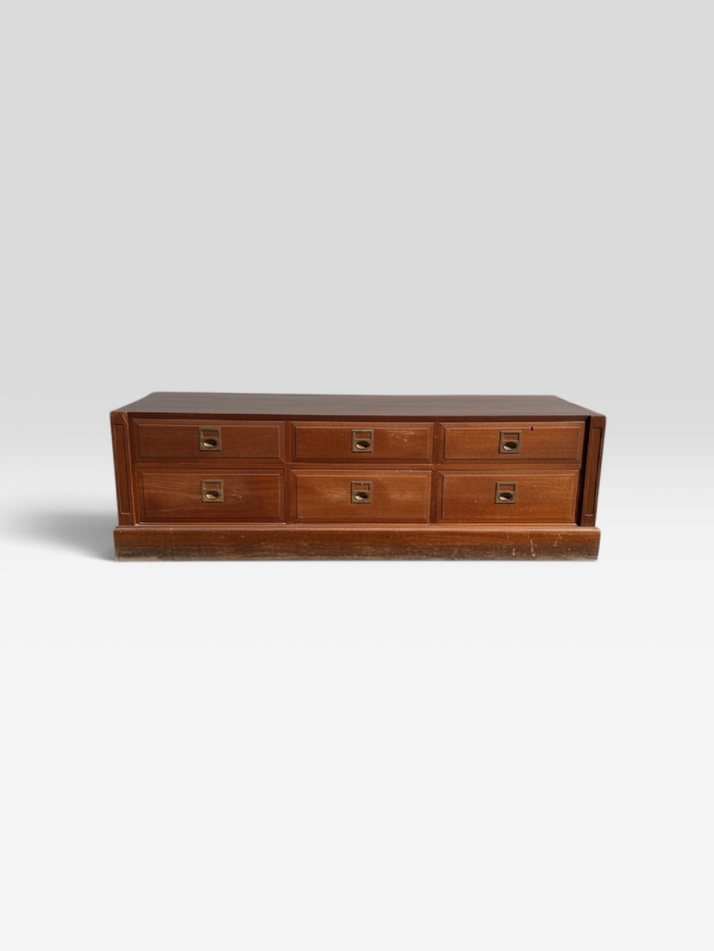 A low-profile mahogany bank of six drawers featuring brass label handles set into a moulded frame with a plinth base.