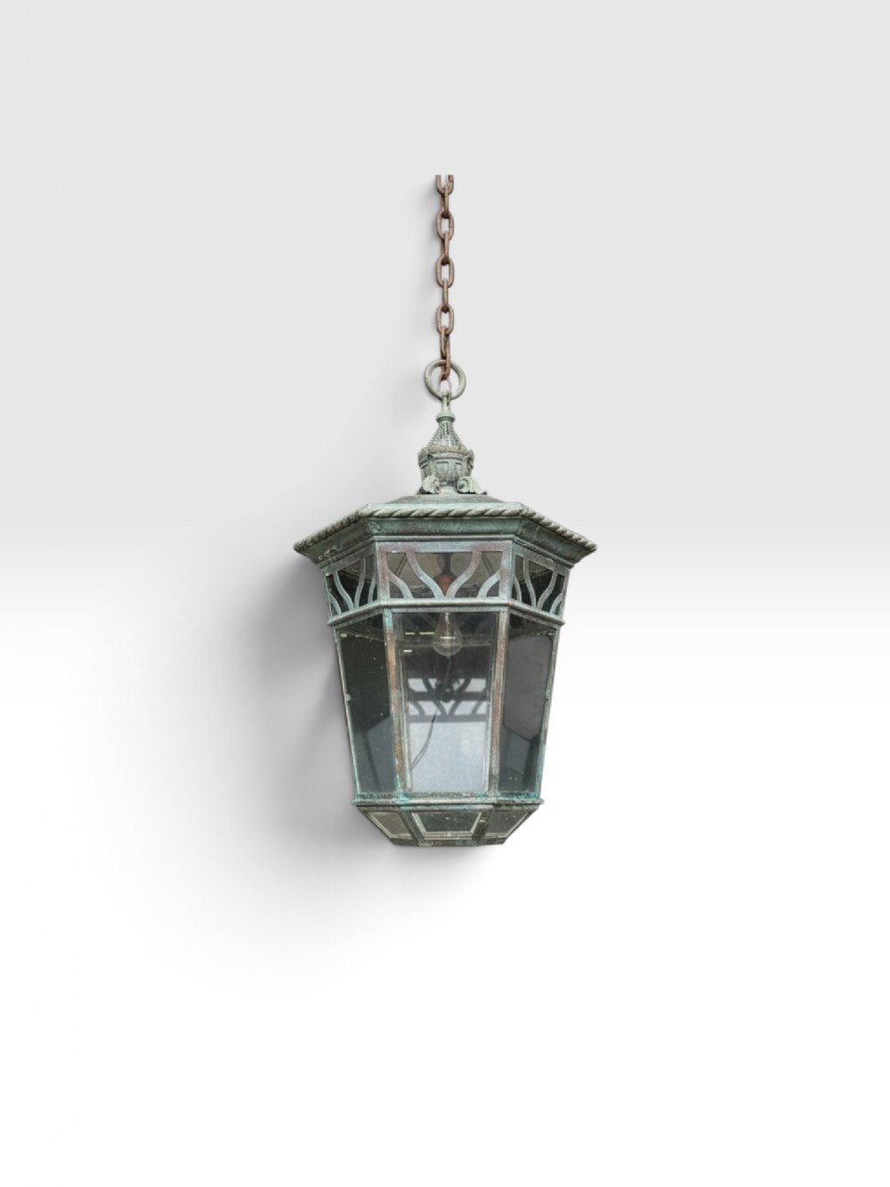 A large 19th-century hexagonal copper lantern with clear glass panels, decorative cut-out detailing, and a natural verdigris patina suspended from a link chain.