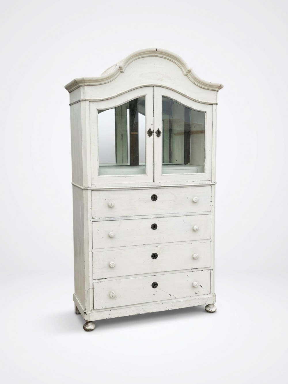 A nineteenth-century Swedish painted off-white bonnet top cabinet with upper glazed doors sitting atop four wide drawers.