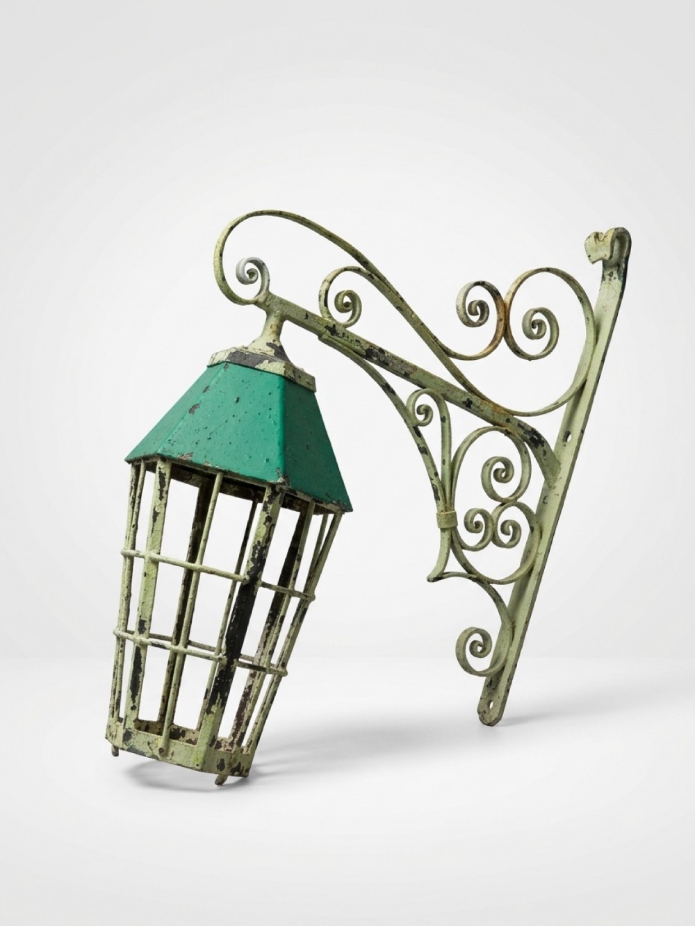 A 19th-century green-painted copper wall lantern suspended from an ornate wrought iron scrollwork bracket.