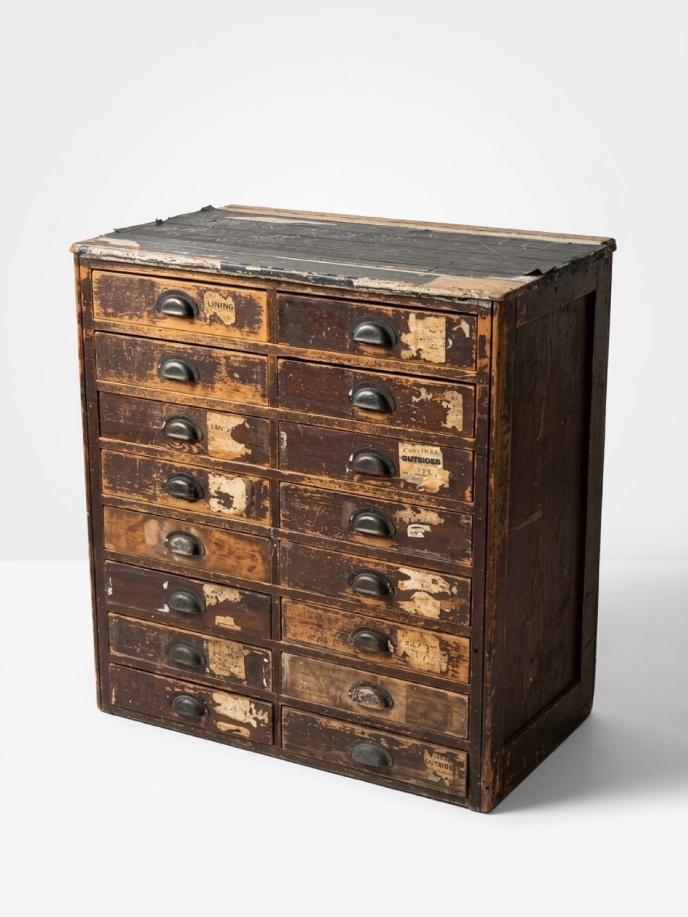 A tall distressed dark wood bank of sixteen drawers featuring metal cup handles and remnants of original paper labels.