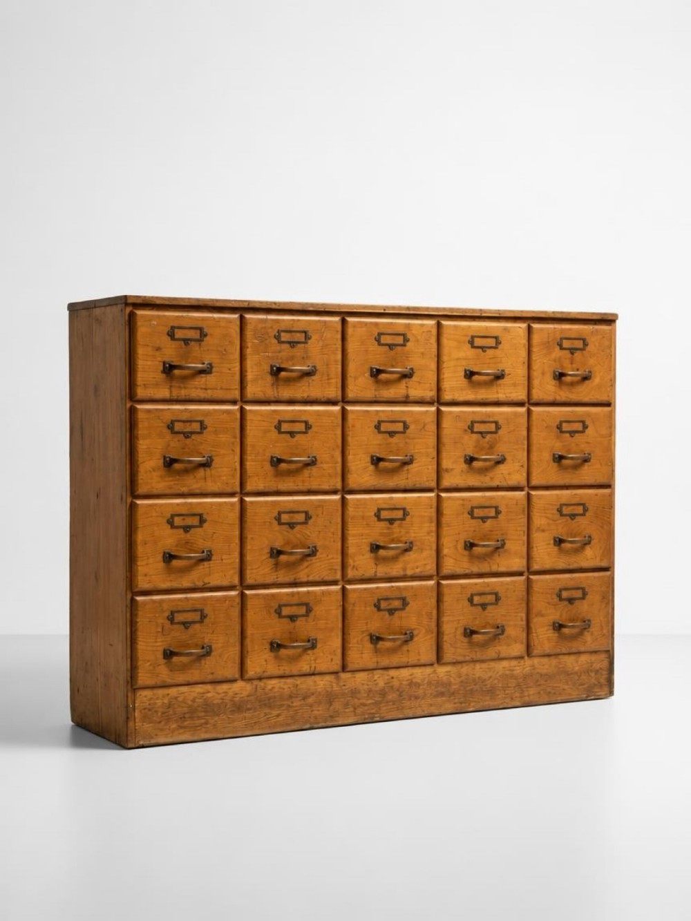 A freestanding wooden bank of twenty drawers featuring brass label holders and metal pull handles resting on a solid plinth base.