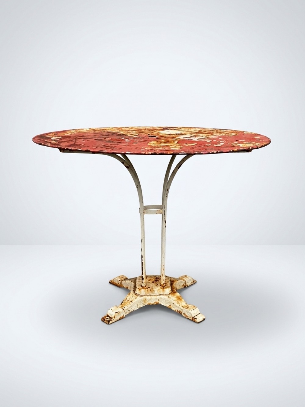 A round French garden table with a distressed red painted top supported by a painted cream metal base with a quadruped pedestal.