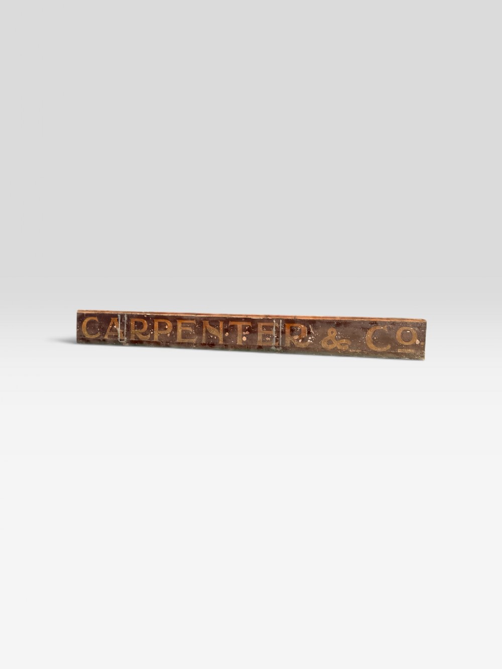 A long, narrow nineteenth-century wooden trade sign featuring a dark brown background with gilded serif lettering reading CARPENTER & CO.