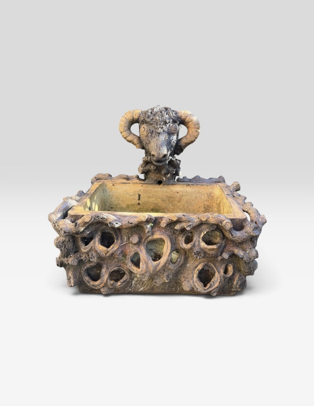 A 19th-century salt-glazed stoneware trough featuring sculpted faux-bois branch texture and a central ram head motif.