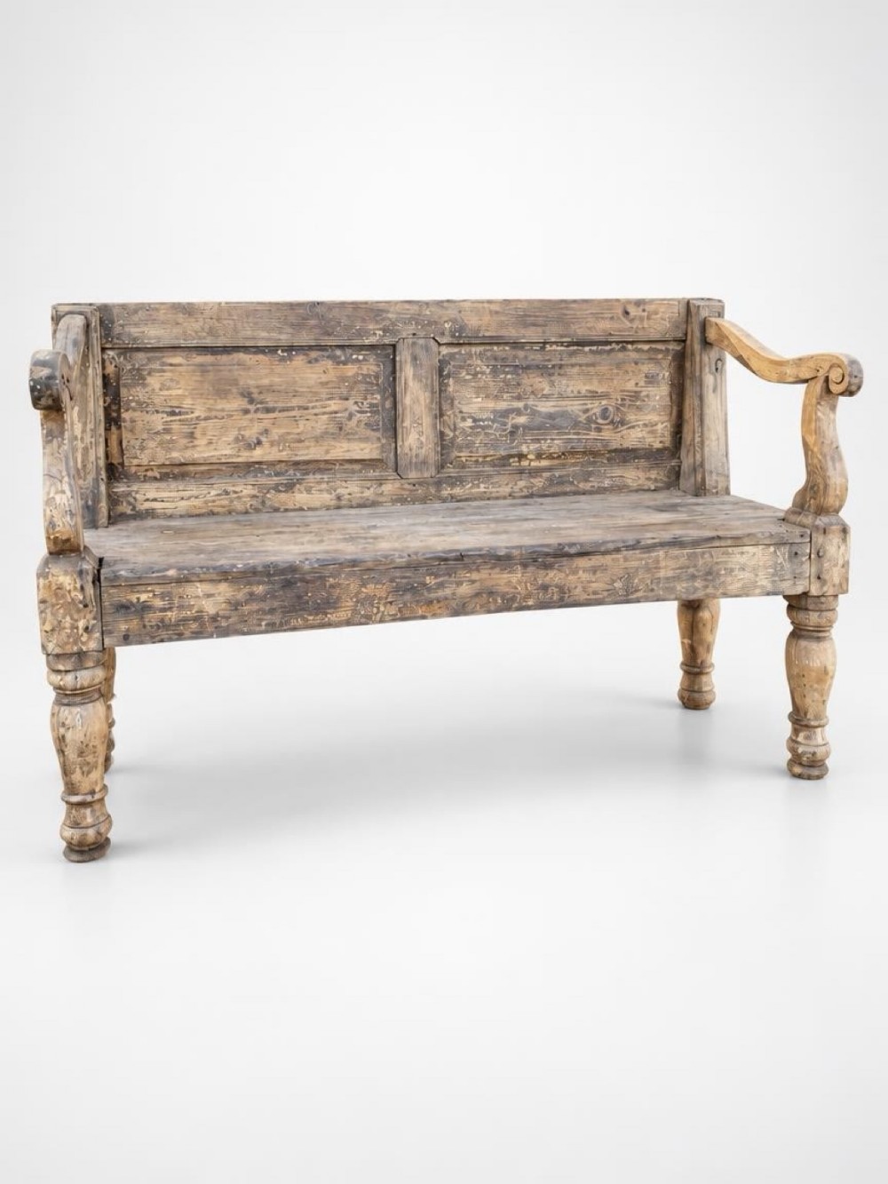 A 19th-century Irish pine wooden bench featuring a twin-panelled backrest, shaped scroll armrests, and turned front legs with a weathered surface.