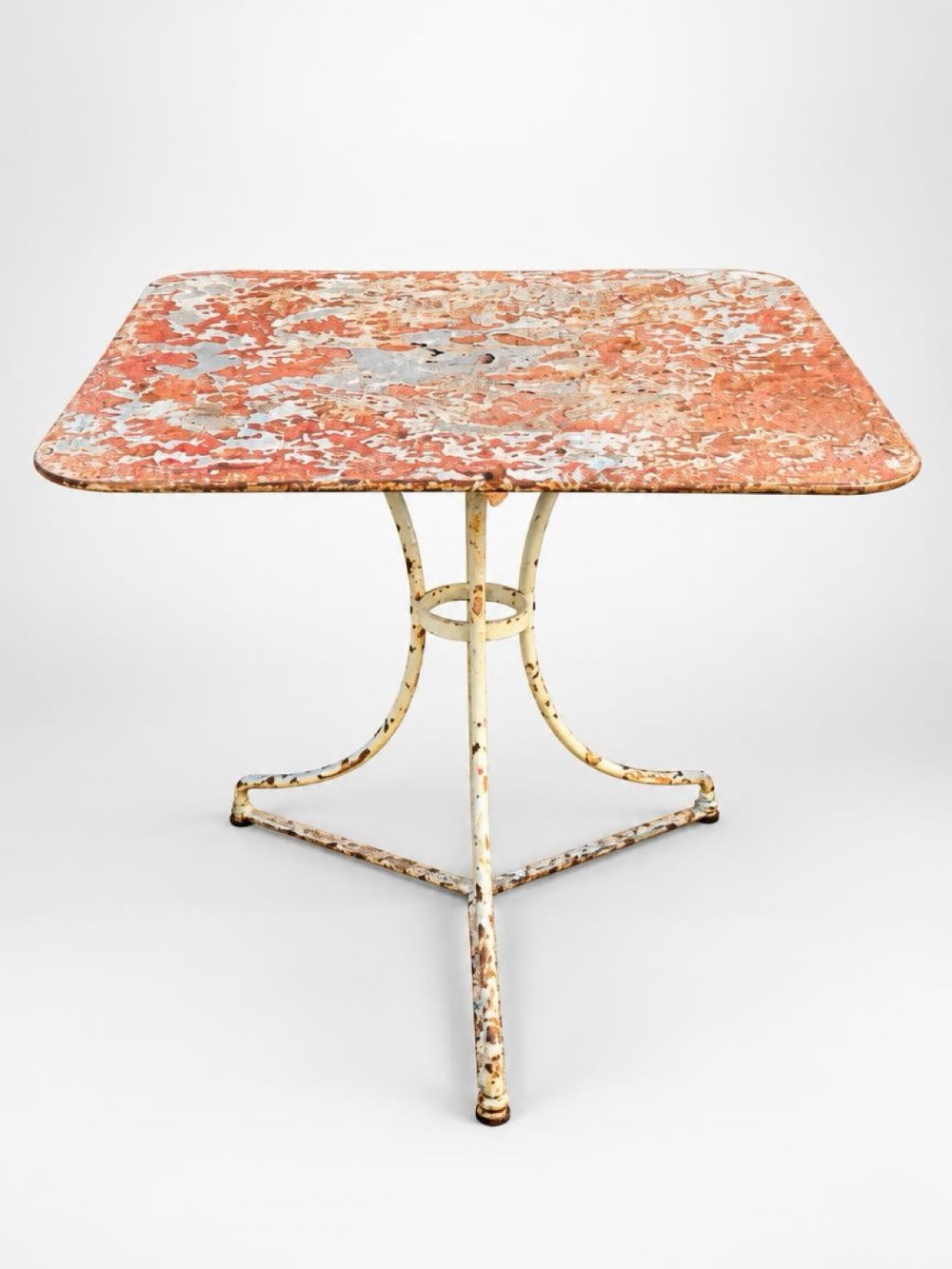 A square vintage French metal bistro table featuring a distressed orange and white painted top supported by a cream-painted tripod iron base.