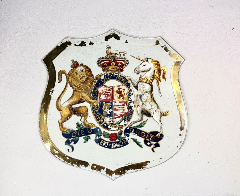 An Edwardian heraldic shield-shaped plaque featuring the gilded British Royal Coat of Arms with a lion, unicorn, and mottoes against a painted off-white background with distressed gold trim. View V