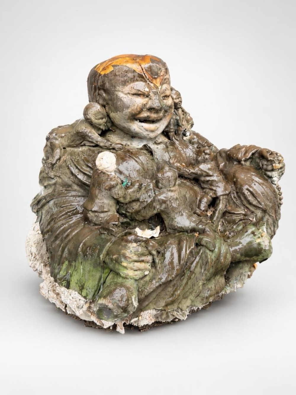 A large glazed plaster sculpture depicting a seated laughing Buddha surrounded by small children in shades of green, brown, and off-white.