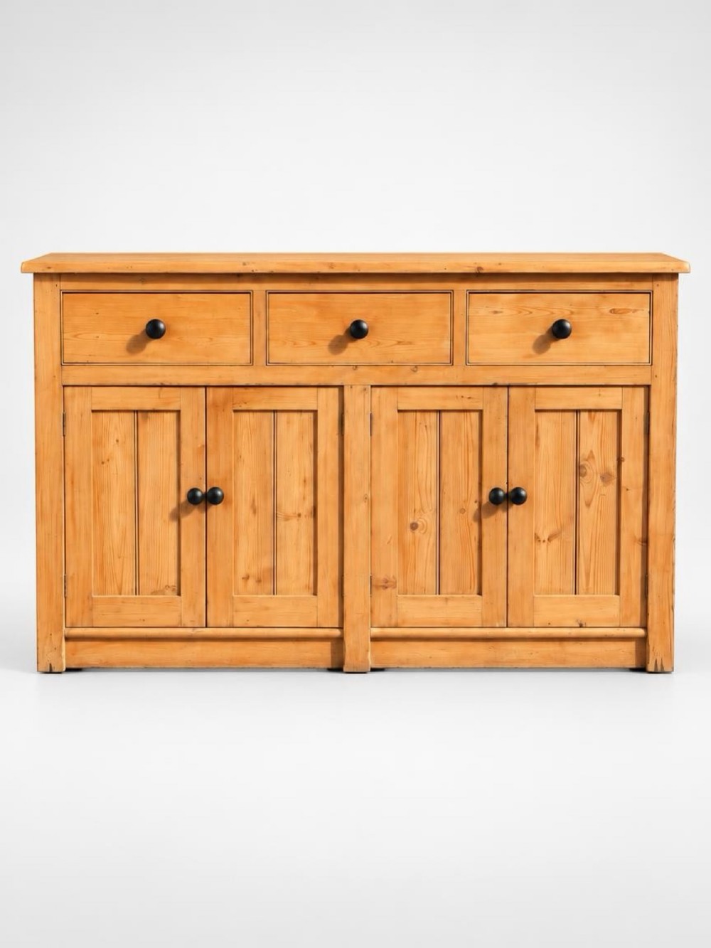 A 19th-century pine dresser base featuring three upper drawers, four panelled cupboard doors, and black turned wooden knobs.