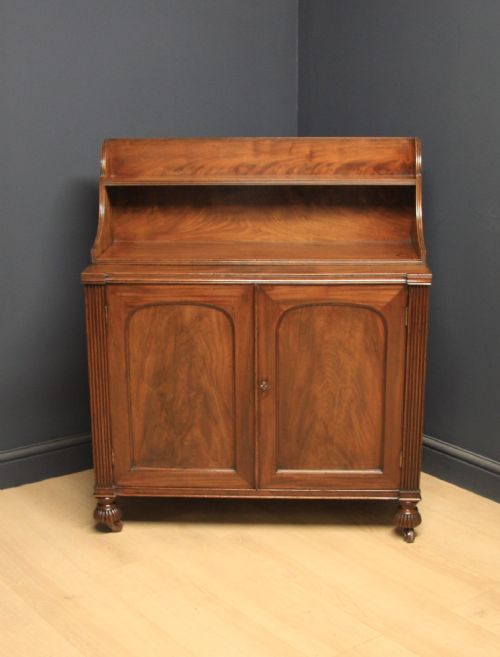 fig 1. A William IV mahogany sideboard featuring a raised back shelf, flame mahogany panelled cupboard doors, reeded side pilasters, and carved turned feet.