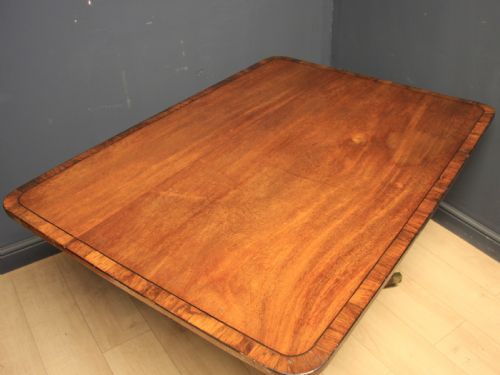 fig 1. A Georgian mahogany pedestal dining table featuring a rectangular crossbanded top supported by a central turned column and four splayed legs with brass castors.