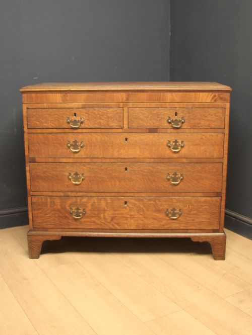 fig 1. A Georgian oak chest of drawers featuring two short over three long drawers with brass swan-neck handles and bracket feet.