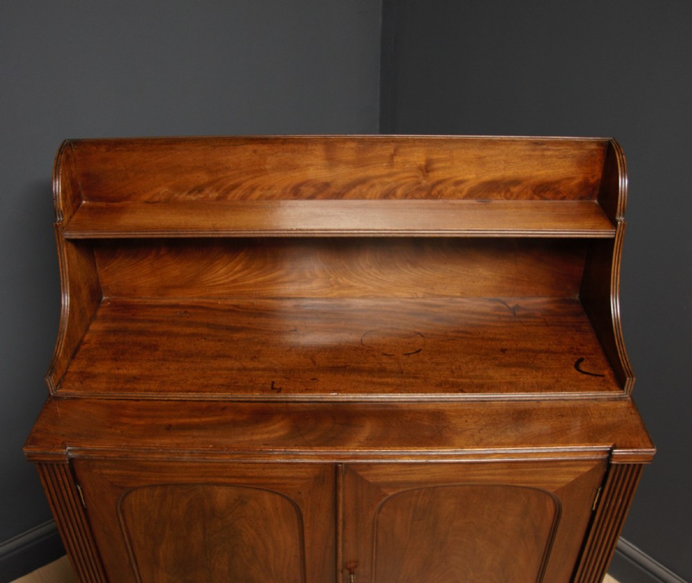 A William IV mahogany sideboard featuring a raised back shelf, flame mahogany panelled cupboard doors, reeded side pilasters, and carved turned feet. View IV