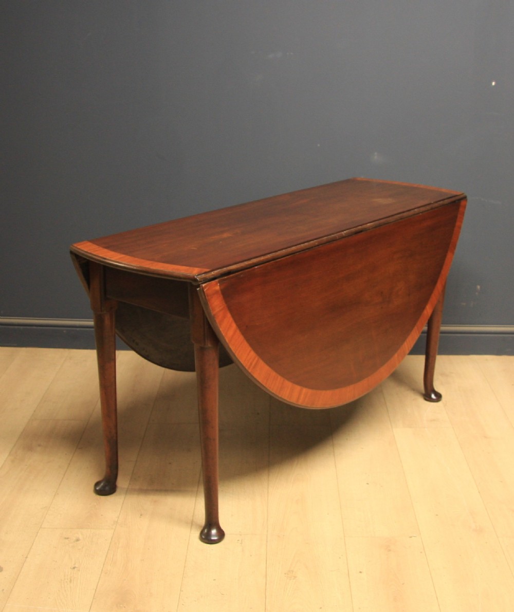A Georgian mahogany drop-leaf dining table featuring crossbanded inlay borders, tapered legs, and pad feet.
