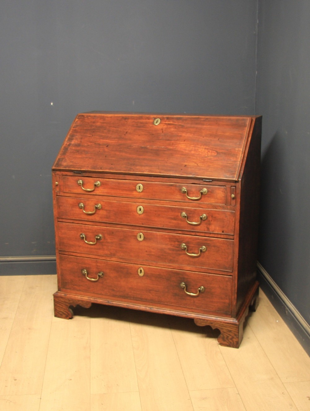 A Georgian elm writing bureau featuring a sloped fall-front flap above four long graduated drawers fitted with brass swan-neck handles, supported on bracket feet.