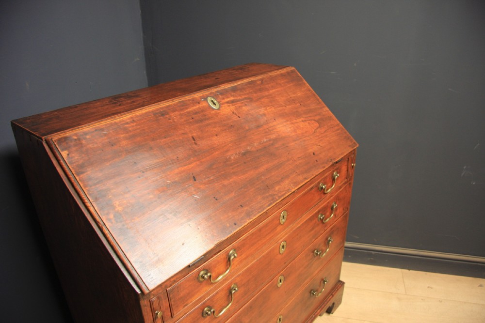 A Georgian elm writing bureau featuring a sloped fall-front flap above four long graduated drawers fitted with brass swan-neck handles, supported on bracket feet. View III