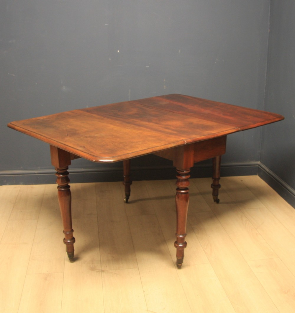 A Victorian warm brown mahogany drop-leaf dining table featuring turned legs and brass castors.