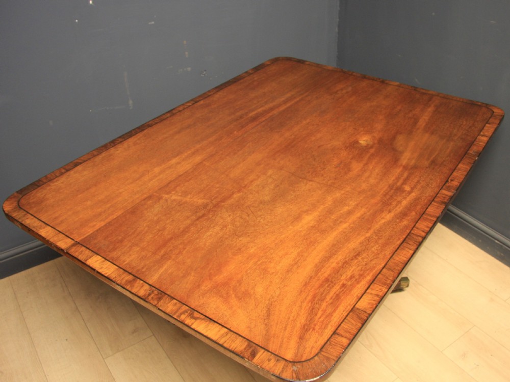 A Georgian mahogany pedestal dining table featuring a rectangular crossbanded top supported by a central turned column and four splayed legs with brass castors. View II