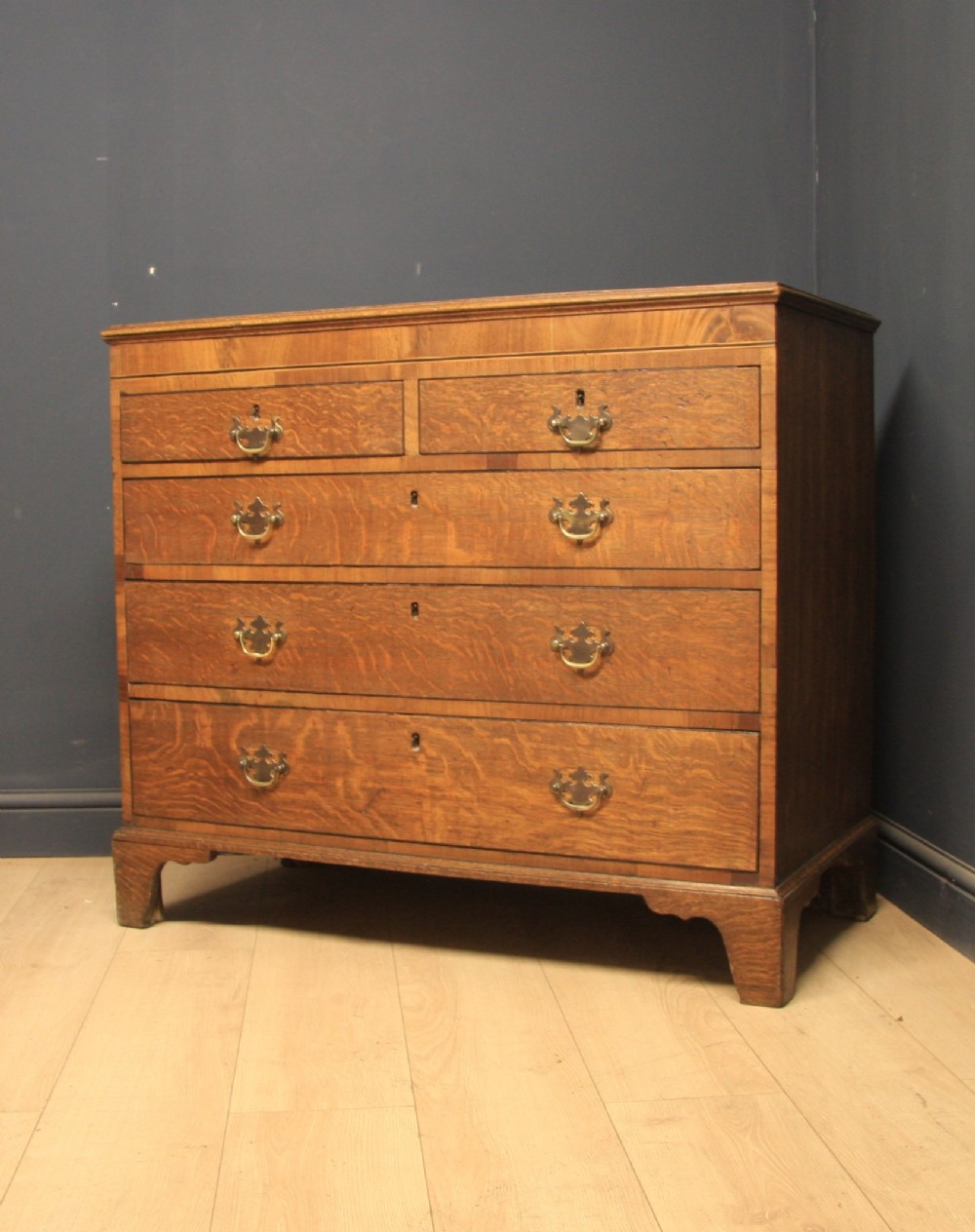A Georgian oak chest of drawers featuring two short over three long drawers with brass swan-neck handles and bracket feet.