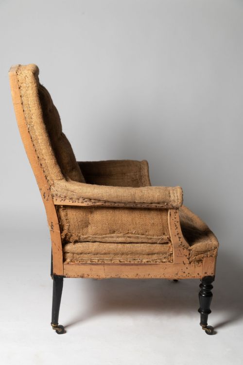 fig 1. An antique French armchair and matching footstool covered in coarse beige hessian upholstery with black turned wooden legs on castors.