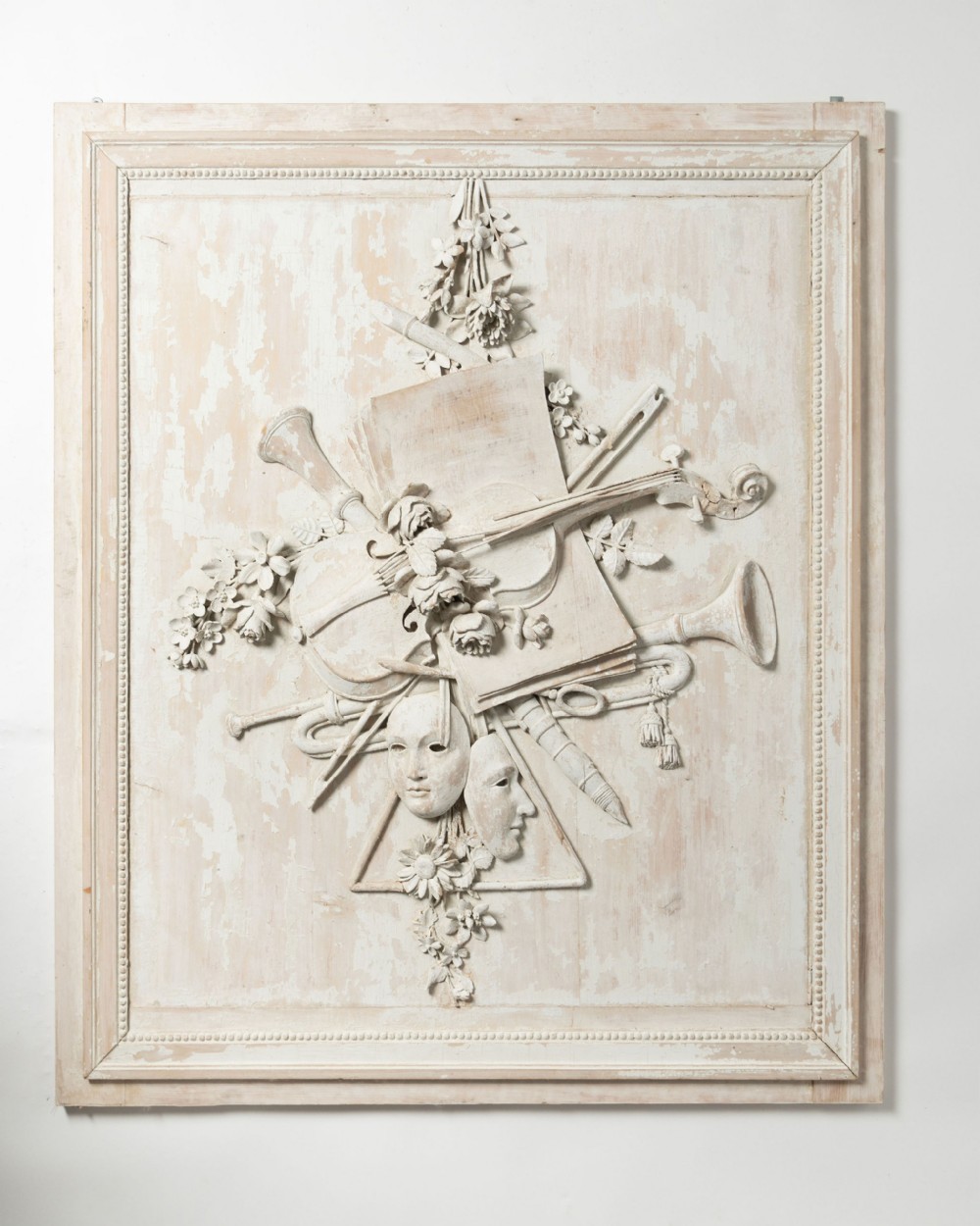 An off-white rectangular wall panel with high-relief carvings of musical instruments, theatrical masks, sheet music, and flowers in a distressed painted finish.