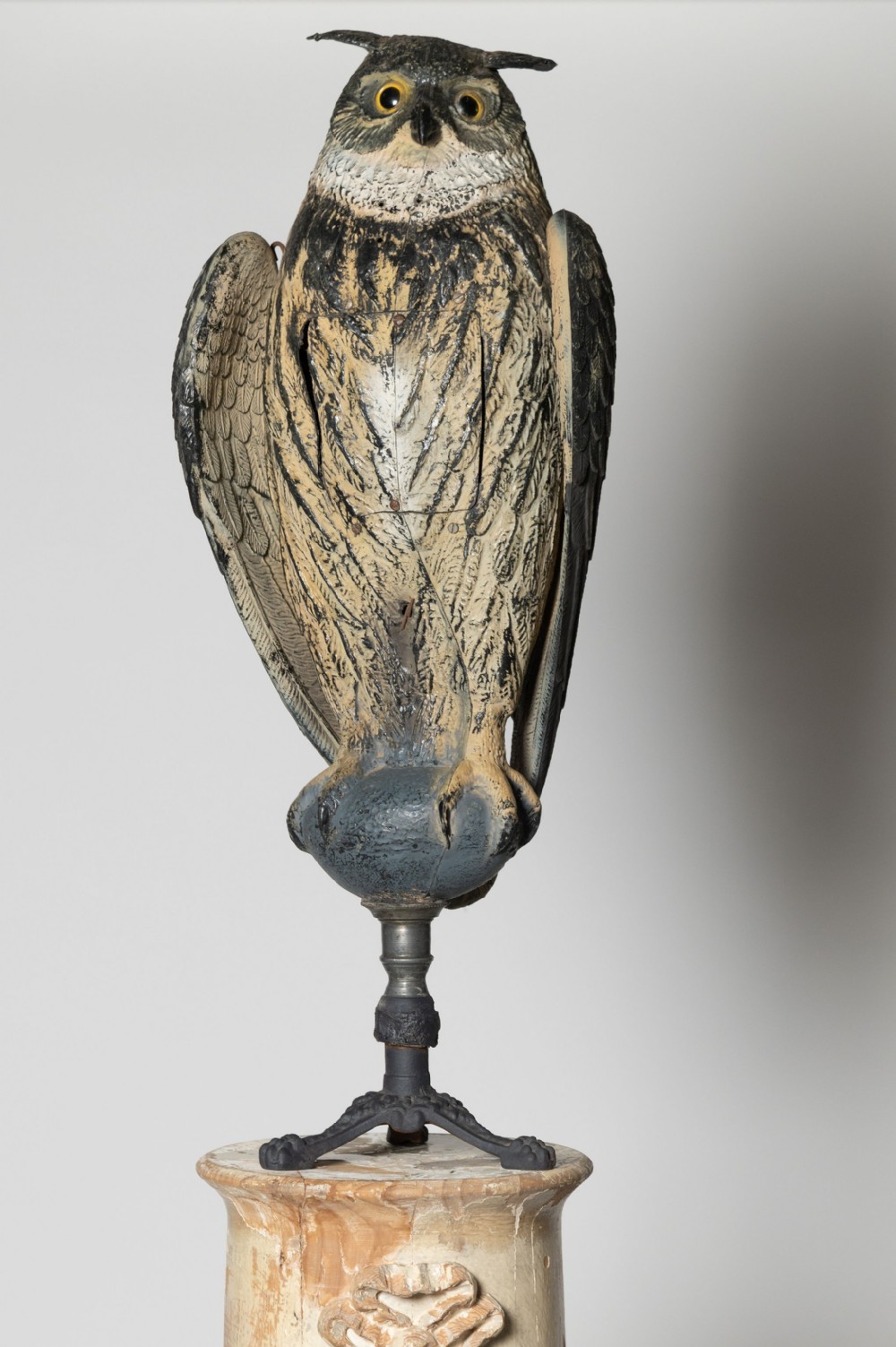 A painted owl decoy sculpture with glass eyes, mounted on a dark metal stem with a tripod base.