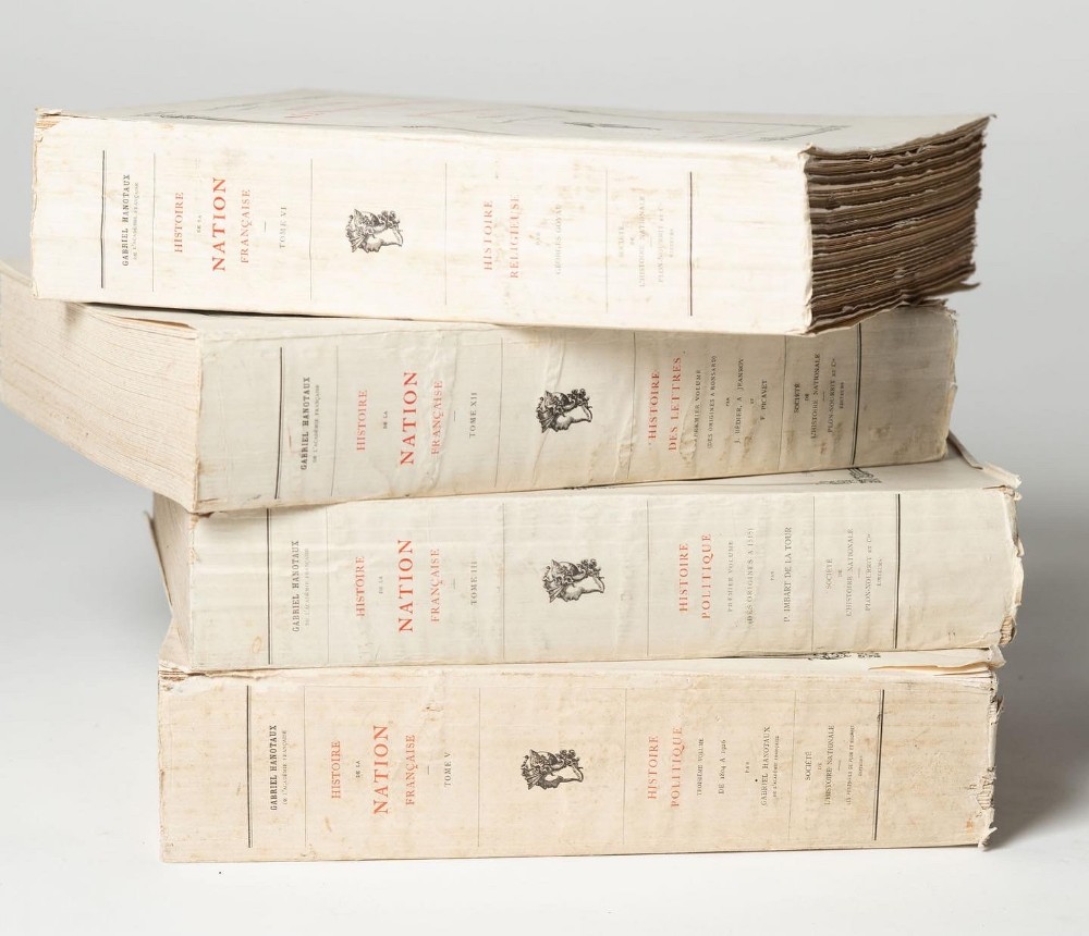 A stacked set of four large antique French history books bound in cream paper spines with printed red and black typography.