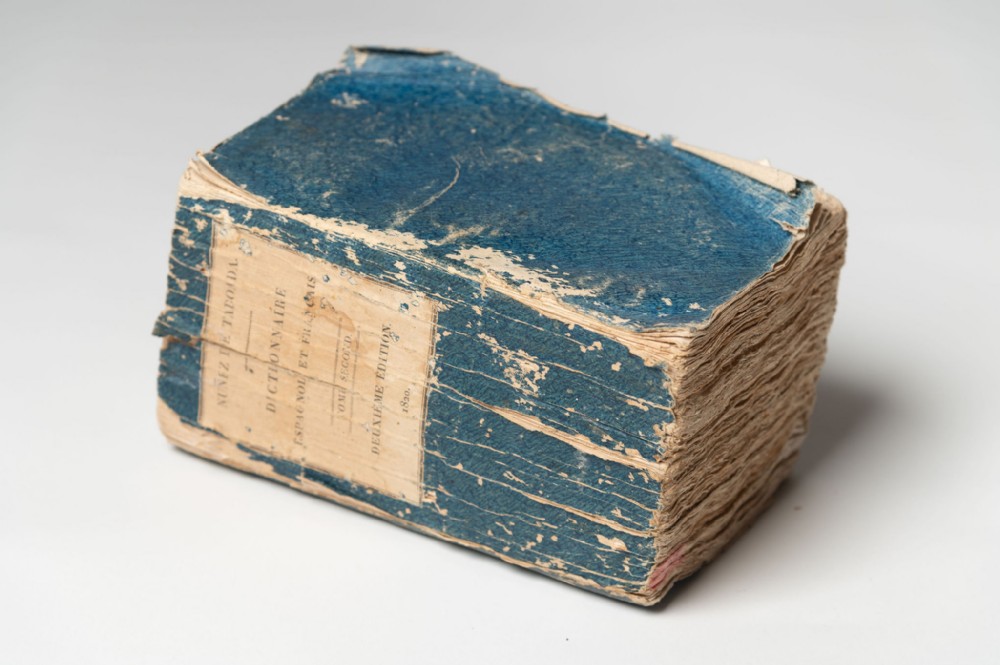 A thick 1820 antique French dictionary featuring a distressed blue paper cover and printed paper label.