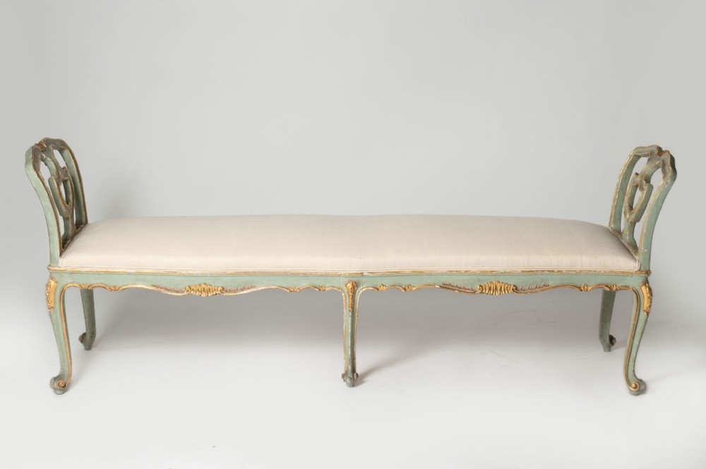 A long Italian Rococo style stool with a pale green and parcel-gilt wooden frame, six cabriole legs, openwork pierced end supports, and a cream upholstered seat.