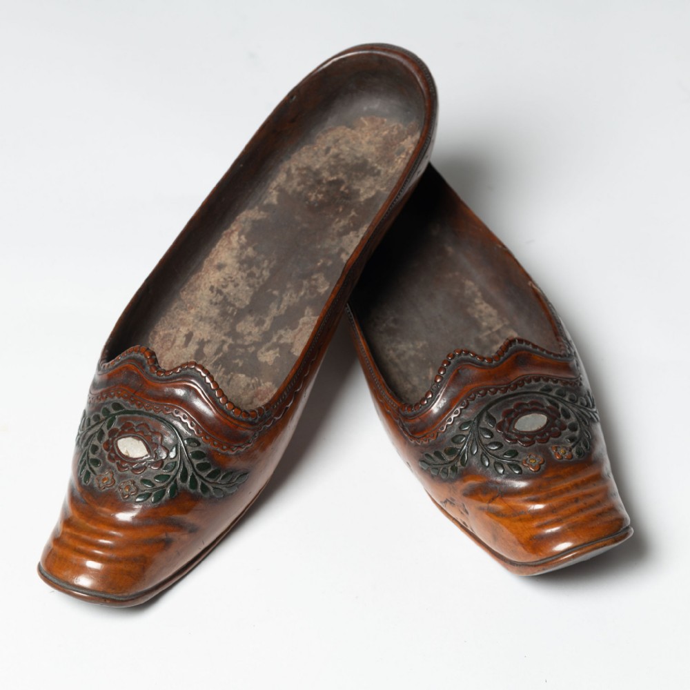 A pair of hand-carved brown wooden shoes featuring raised floral carved vamps with mother-of-pearl inlays and squared toes.