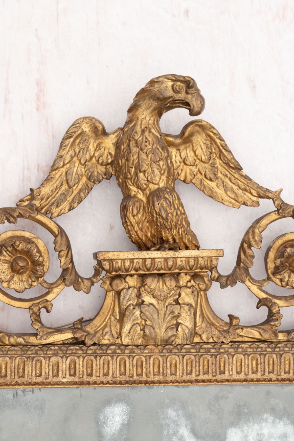 An 18th-century Italian giltwood wall mirror featuring a carved eagle crest, floral side accents, and a patinated two-part mirror plate. View II