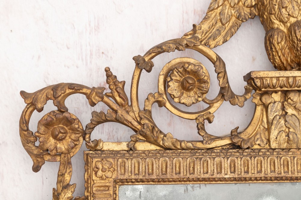An 18th-century Italian giltwood wall mirror featuring a carved eagle crest, floral side accents, and a patinated two-part mirror plate. View IV