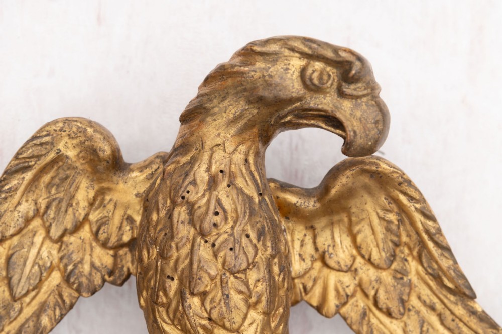 An 18th-century Italian giltwood wall mirror featuring a carved eagle crest, floral side accents, and a patinated two-part mirror plate. View V