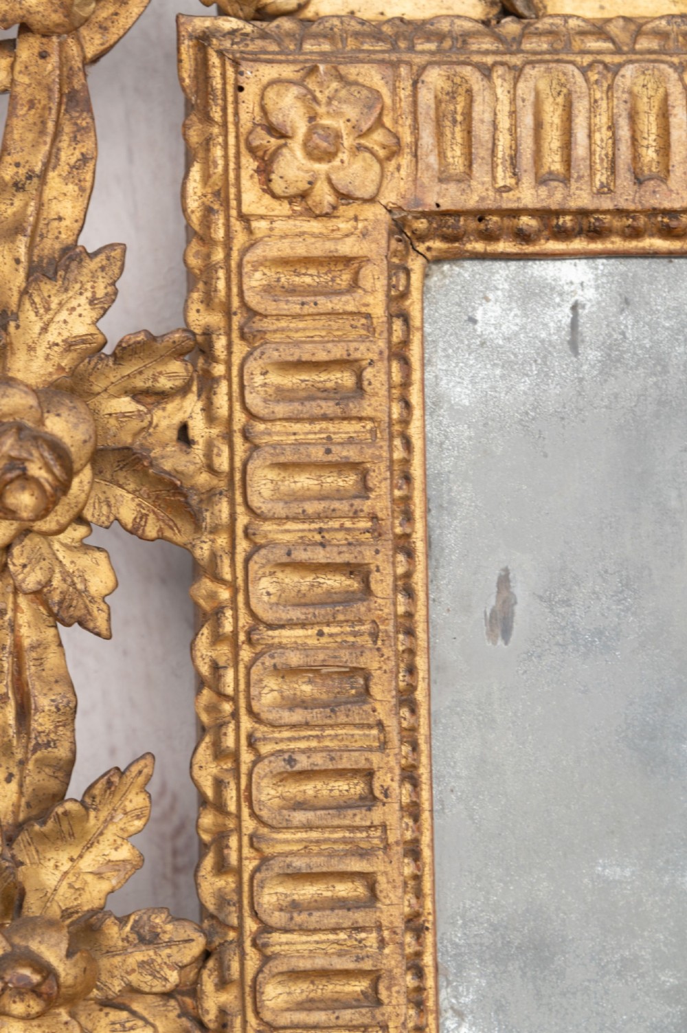 An 18th-century Italian giltwood wall mirror featuring a carved eagle crest, floral side accents, and a patinated two-part mirror plate. View VI