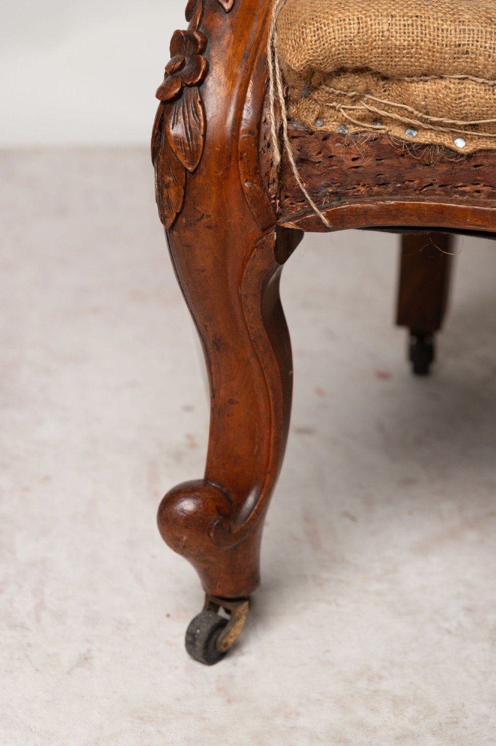 An antique English wingback armchair with carved wooden cabriole legs on castors, upholstered in cream calico with a hessian seat base ready for reupholstery. View IV