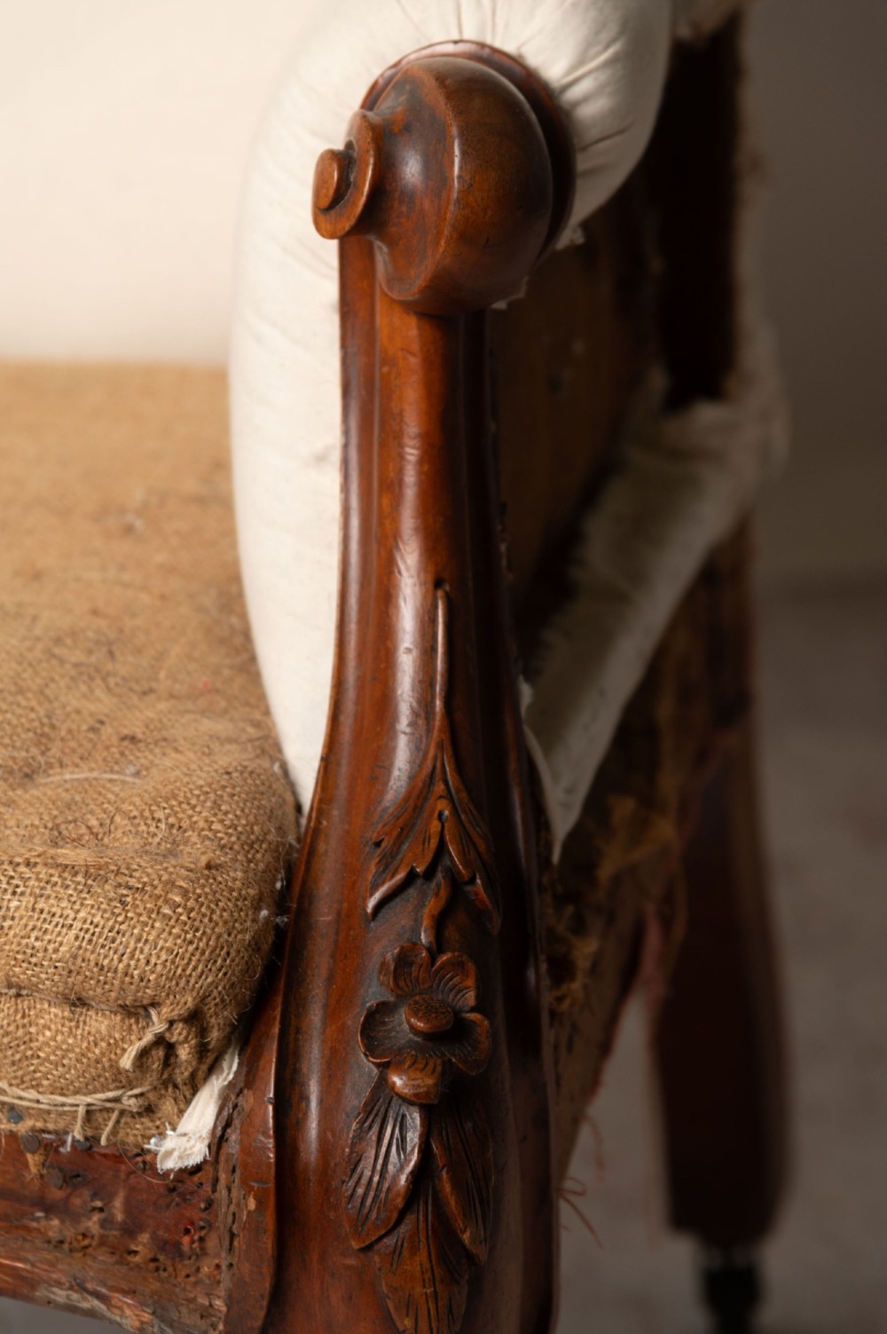 An antique English wingback armchair with carved wooden cabriole legs on castors, upholstered in cream calico with a hessian seat base ready for reupholstery. View V