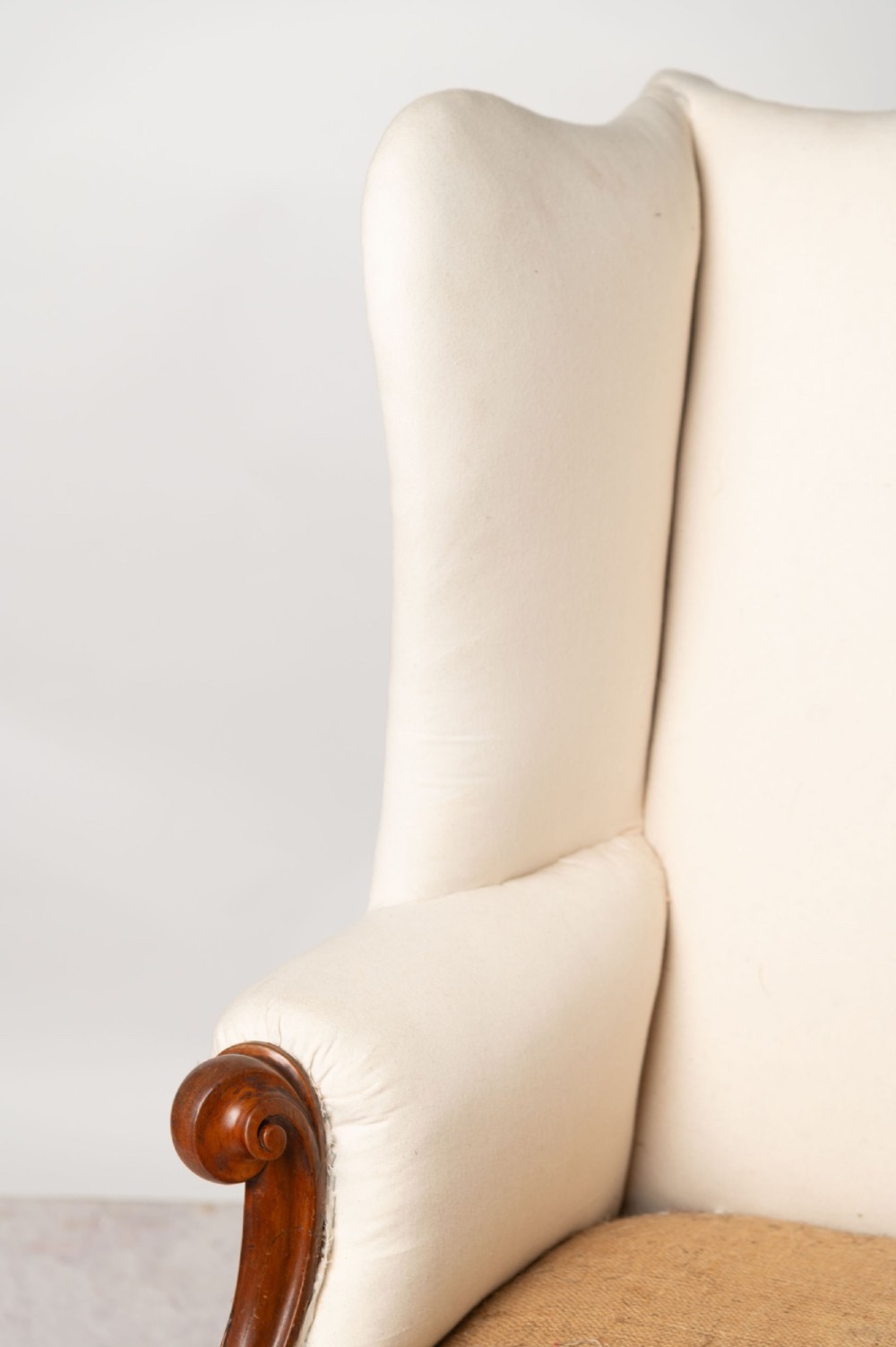 An antique English wingback armchair with carved wooden cabriole legs on castors, upholstered in cream calico with a hessian seat base ready for reupholstery. View VII