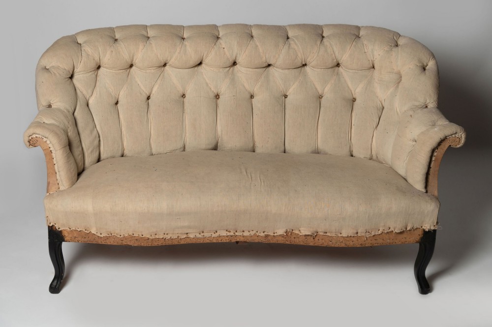 An antique French sofa upholstered in cream calico fabric with deep button tufting along the backrest and dark cabriole front legs.