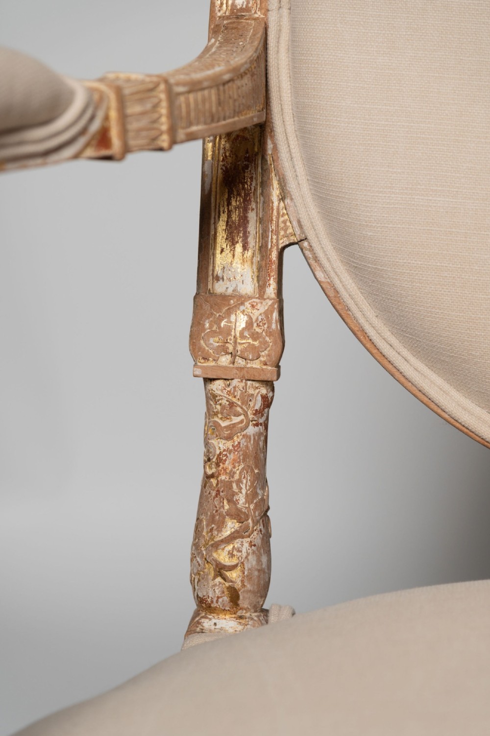 An antique Louis XVI style French settee featuring a distressed gilded wooden frame, oval medallion backrest, and cream linen upholstery. View II