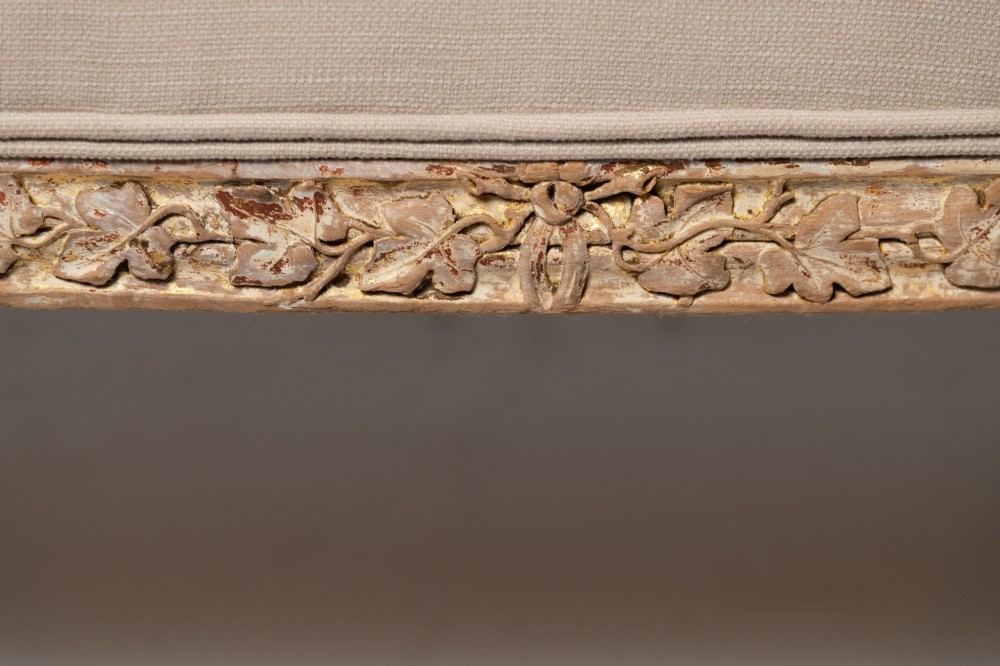An antique Louis XVI style French settee featuring a distressed gilded wooden frame, oval medallion backrest, and cream linen upholstery. View V