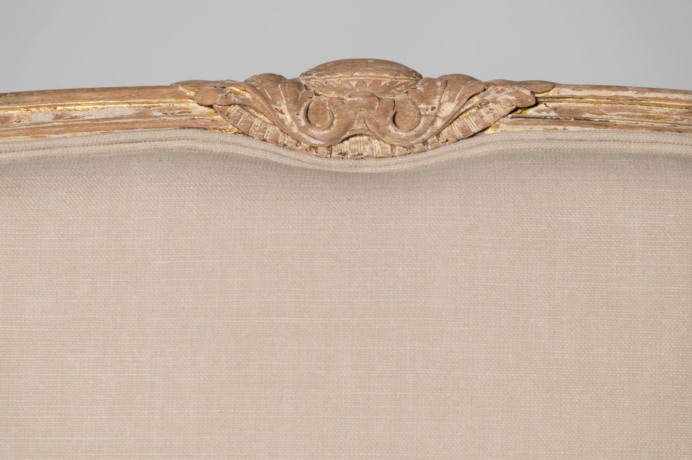 An antique Louis XVI style French settee featuring a distressed gilded wooden frame, oval medallion backrest, and cream linen upholstery. View VI