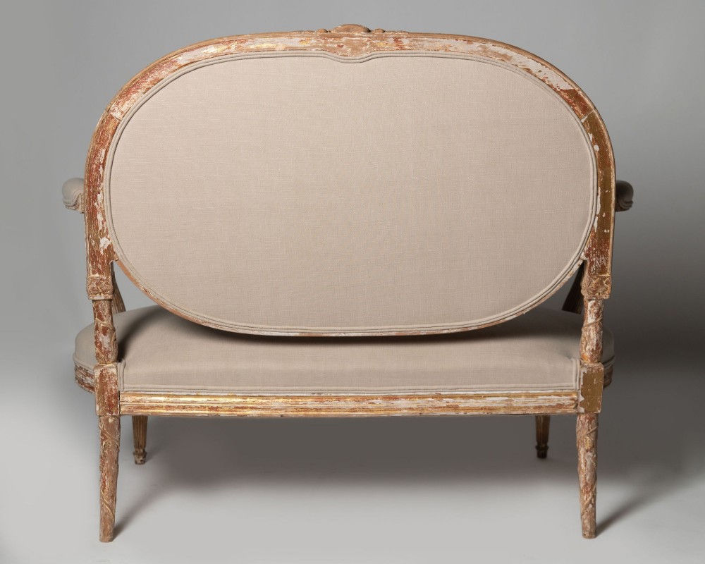 An antique Louis XVI style French settee featuring a distressed gilded wooden frame, oval medallion backrest, and cream linen upholstery. View VIII