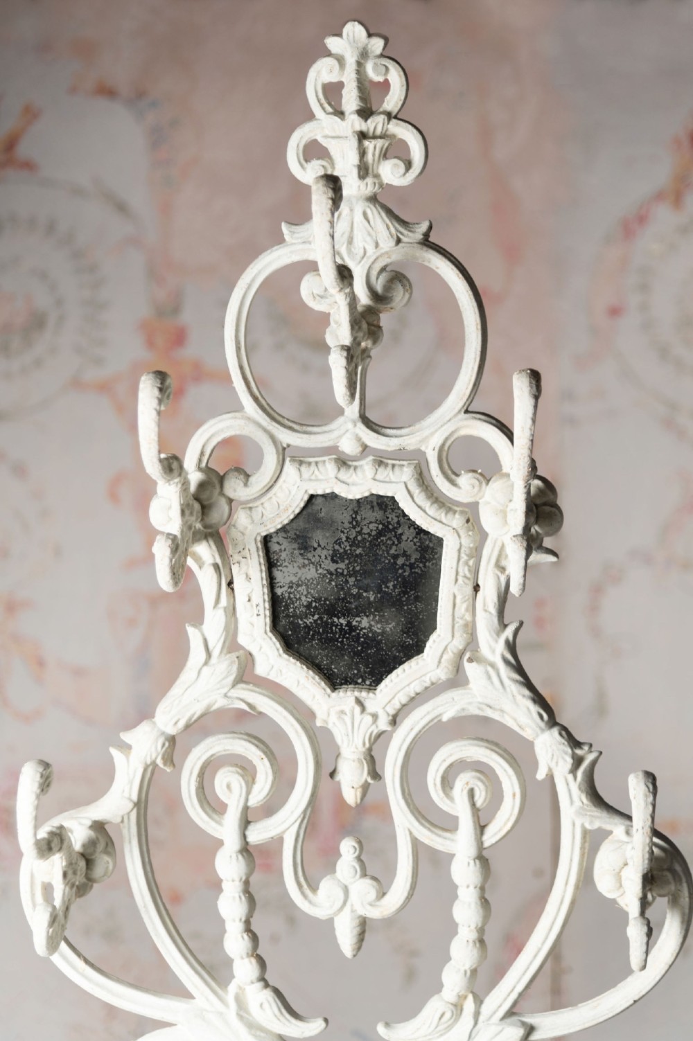 An antique white painted cast iron hall stand featuring intricate scrollwork, integrated coat hooks, a small central mirror, and a base drip tray. View VIII