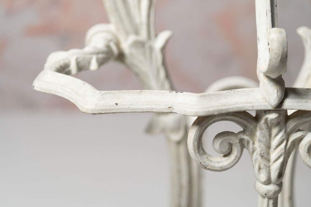 An antique white painted cast iron hall stand featuring intricate scrollwork, integrated coat hooks, a small central mirror, and a base drip tray. View X