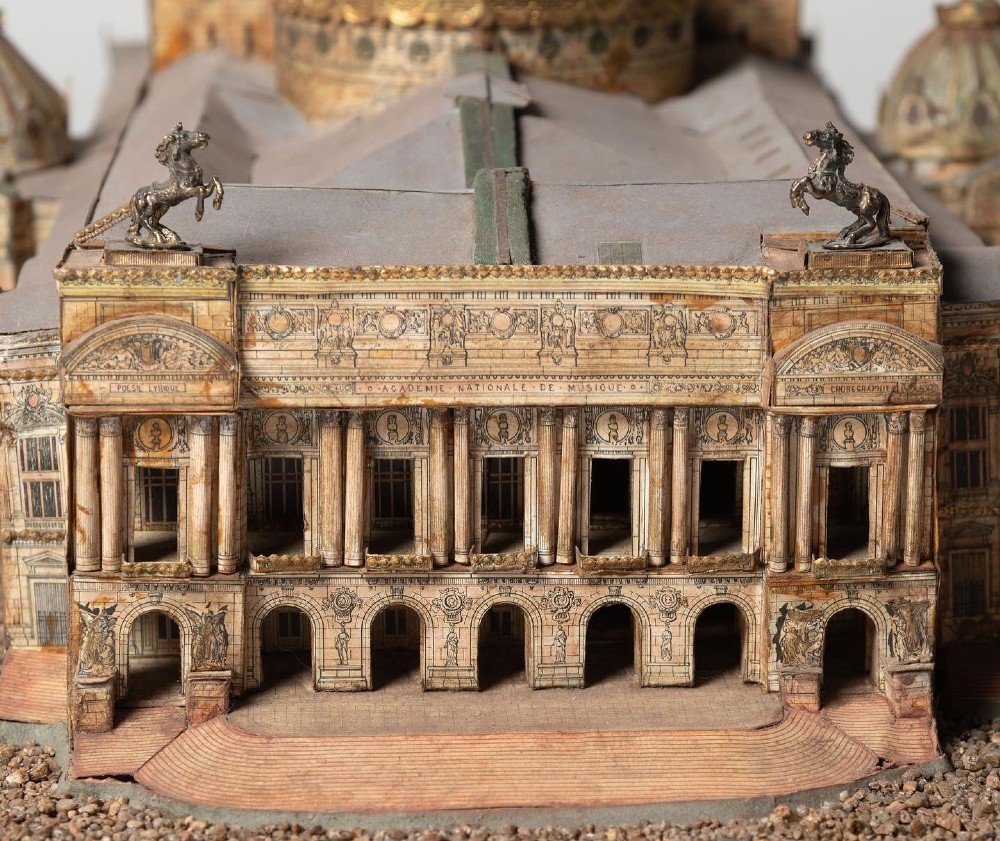 A detailed scale paper model of the Paris Opera House featuring a central dome, classical arcade facade, and miniature roof statuary mounted on a textured gravel base. View II