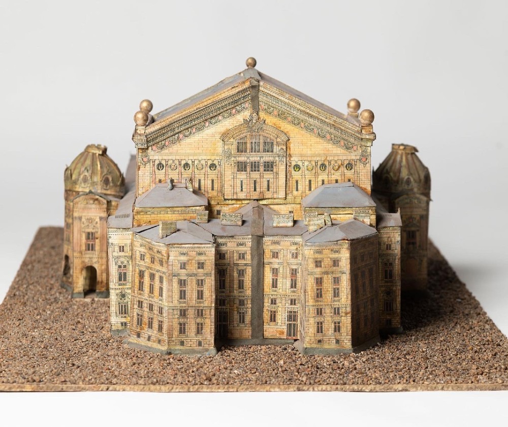 A detailed scale paper model of the Paris Opera House featuring a central dome, classical arcade facade, and miniature roof statuary mounted on a textured gravel base. View VII