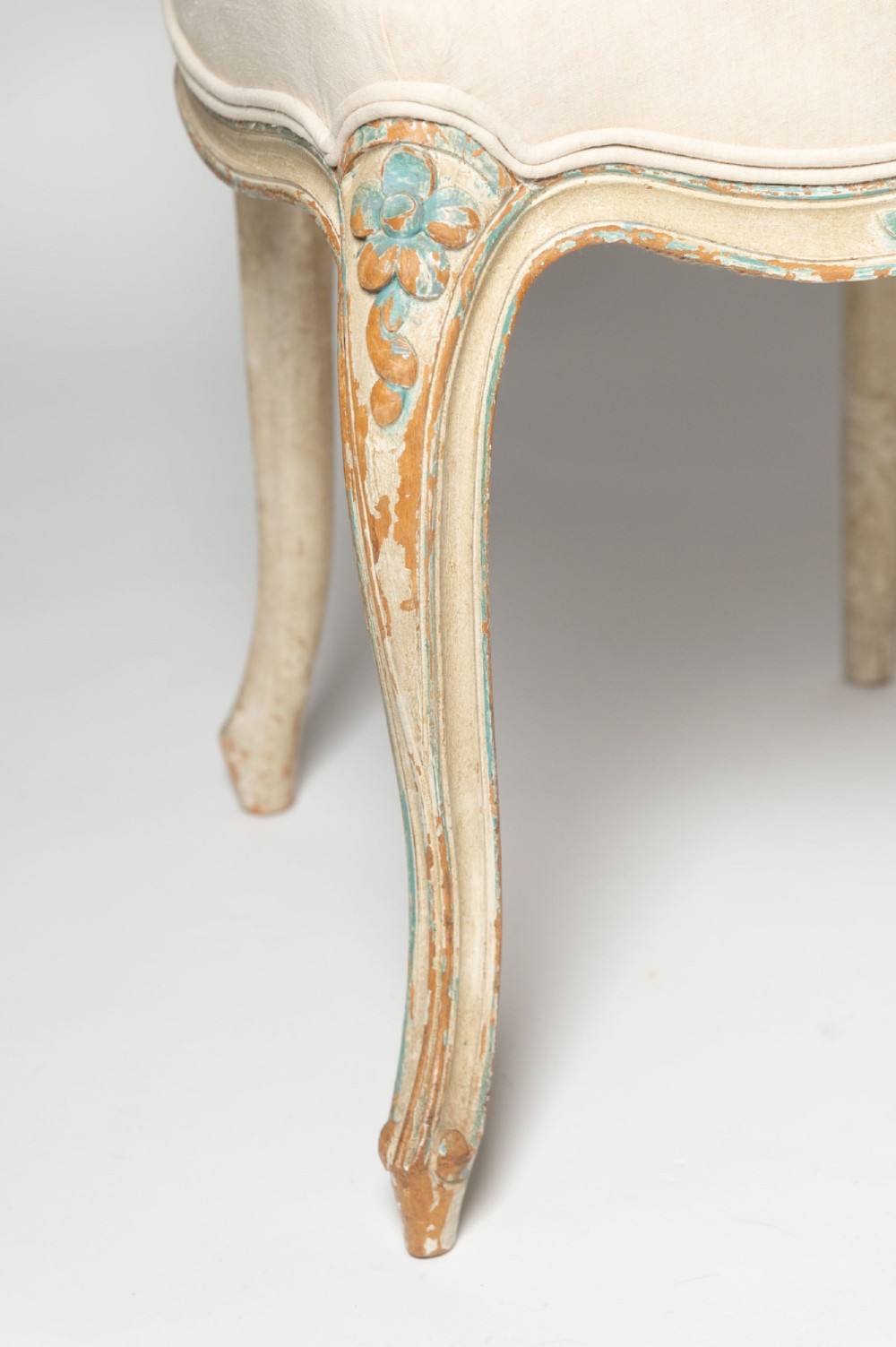 A pair of antique French side chairs featuring distressed off-white painted frames with floral crest carvings, cabriole legs, and neutral linen upholstery. View VII