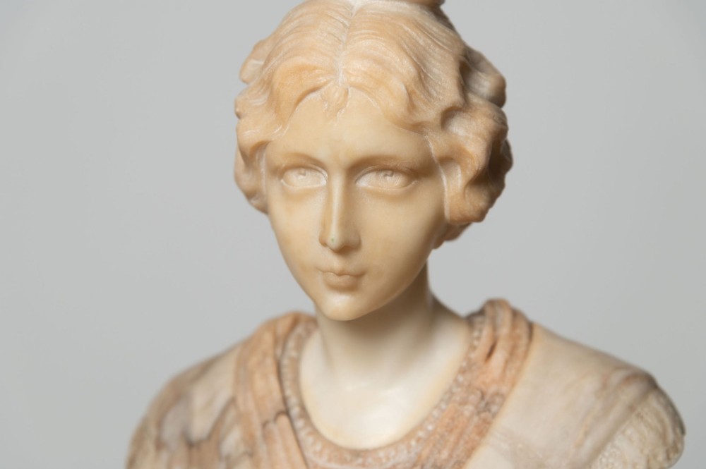 A carved cream alabaster bust depicting a female figure with stylized hair atop a polished turned stone socle. View II