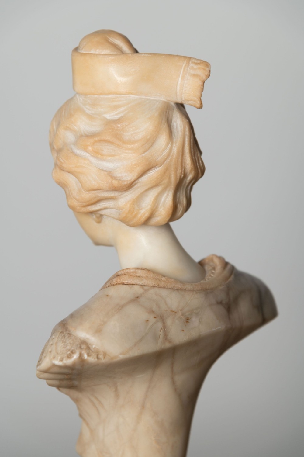 A carved cream alabaster bust depicting a female figure with stylized hair atop a polished turned stone socle. View IV